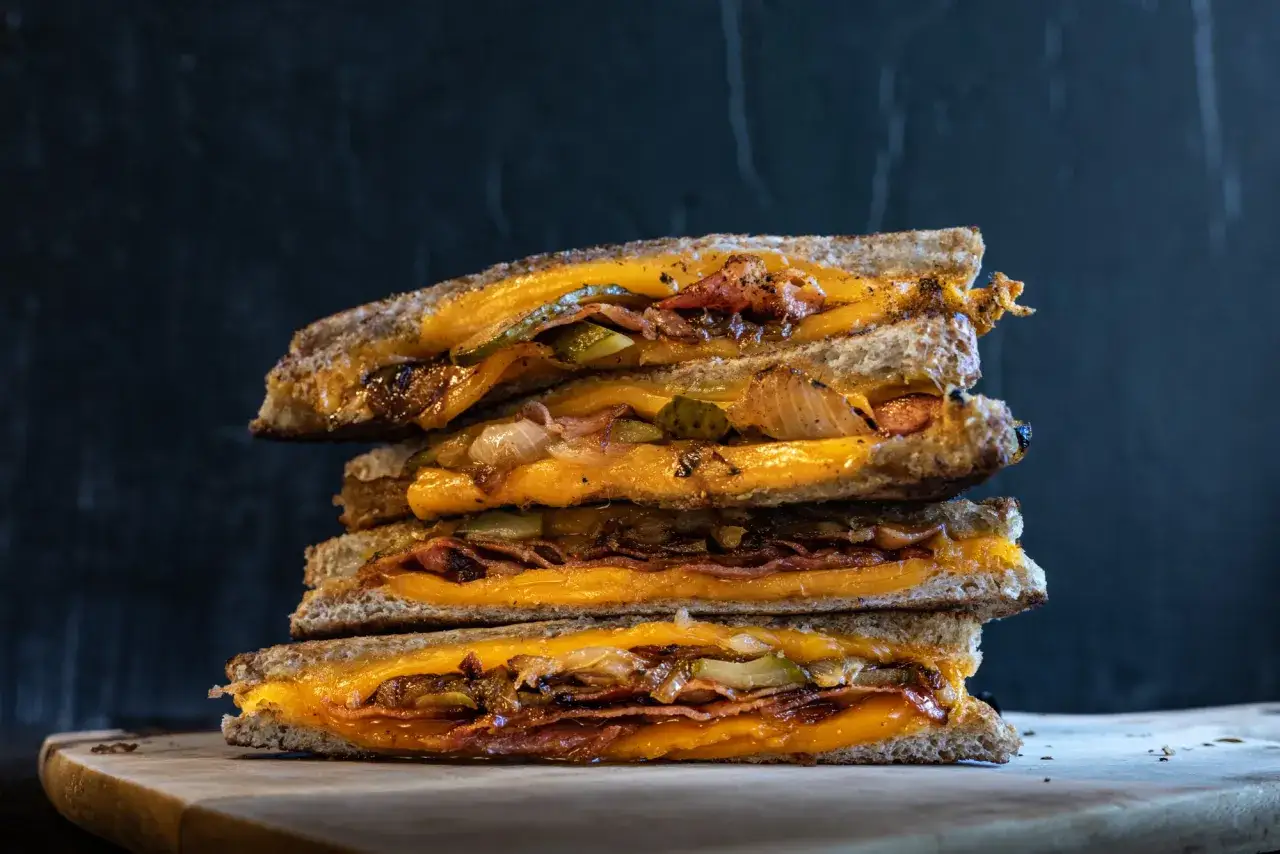 Gestapelte gegrillte Käsesandwiches mit Speck, Gurken und karamellisierten Zwiebeln. Ein köstliches grilled cheese sandwich rezept.