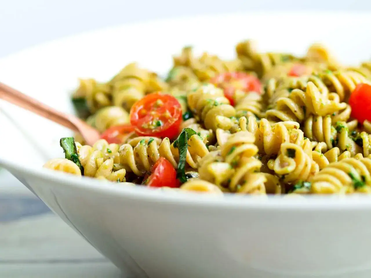 Ein köstlicher nudelsalat mit pesto, garniert mit frischen Kirschtomaten und Basilikum.
