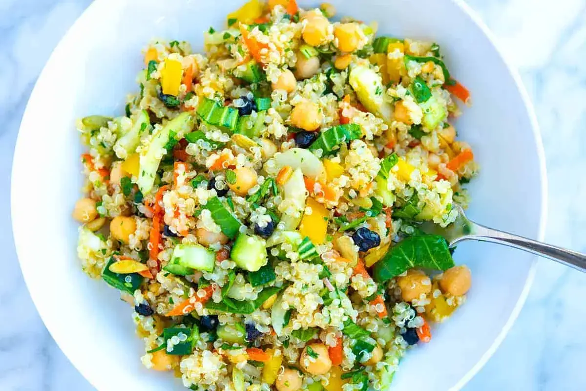 Bunter Quinoa Salat mit Kichererbsen, Gurke, Karotten und Paprika, garniert mit frischer Petersilie.