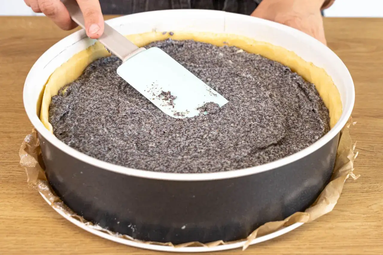 Ein Mohnkuchen mit Puddingfüllung wird in einer Springform glattgestrichen.