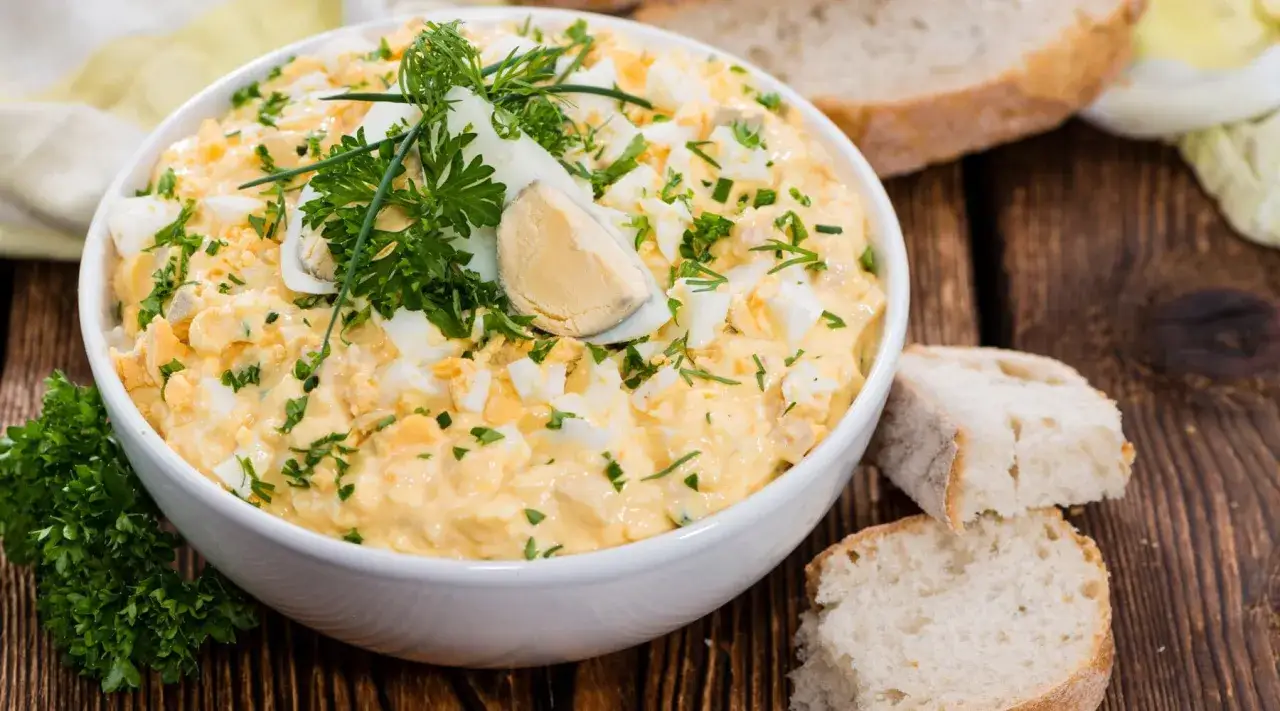 Cremiger eiersalat ohne mayo, garniert mit frischer Petersilie und Dill, serviert mit rustikalem Brot.