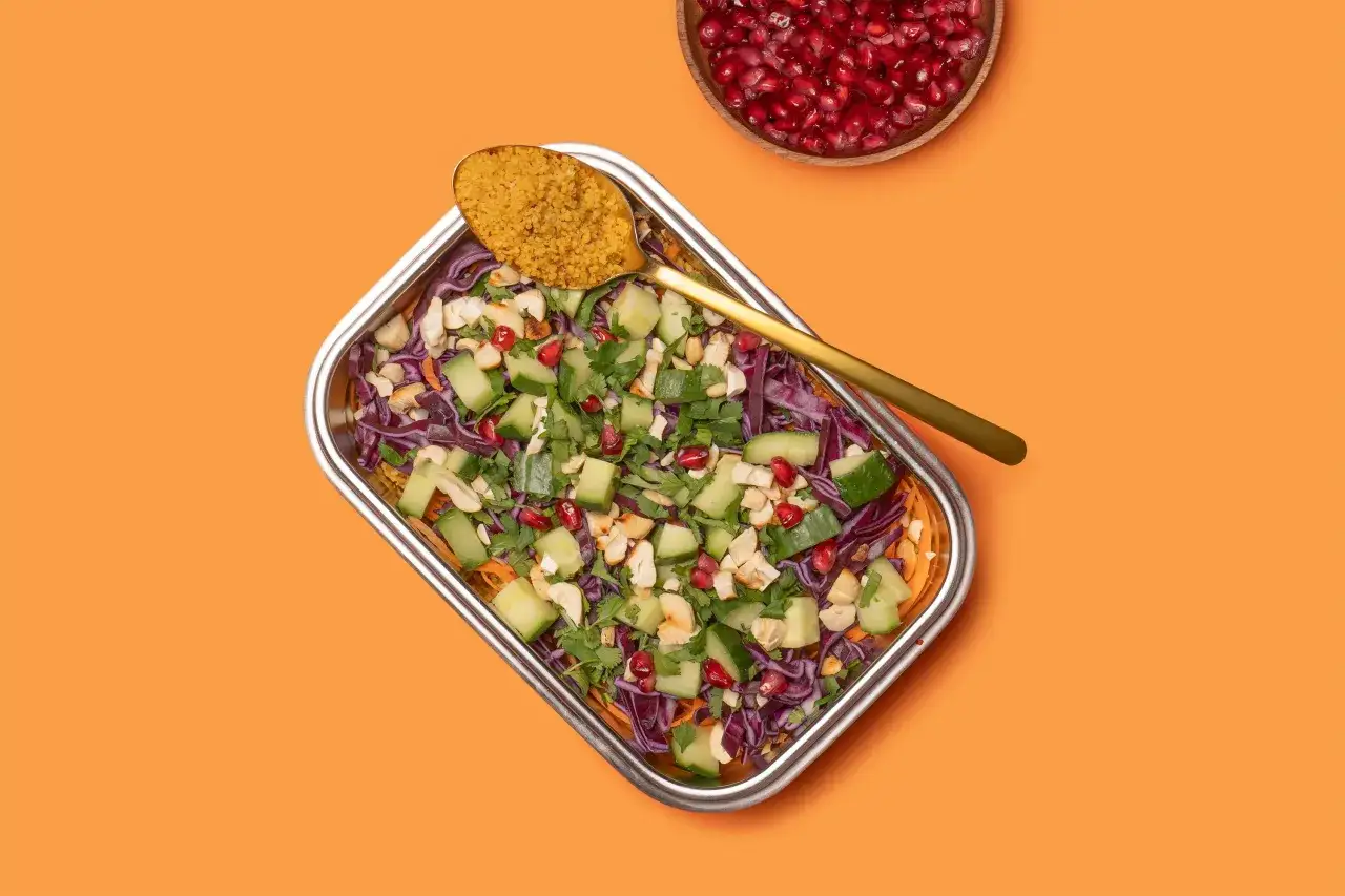 Bunter Couscous-Salat mit Gurken, Granatapfelkernen, Nüssen und Kräutern, garniert mit einer goldenen Löffelportion Couscous.