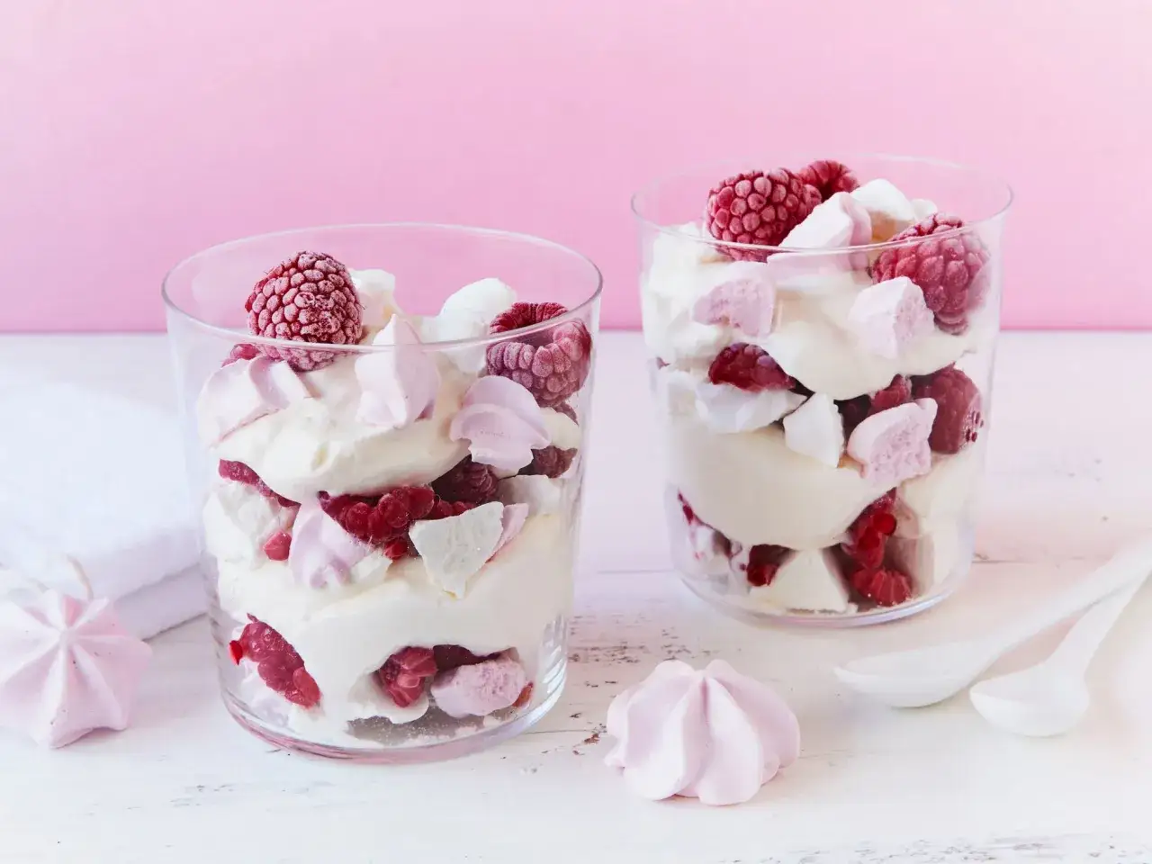 Zwei Gl&auml;ser mit Himbeer Baiser Dessert, geschichtet mit Sahne, frischen Himbeeren und Baiserst&uuml;ckchen.