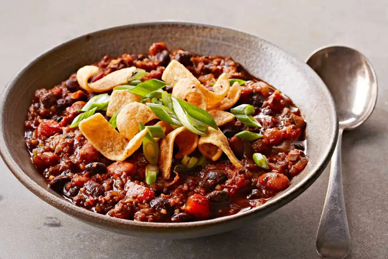 Herzhaftes Chili sin Carne mit schwarzen Bohnen, Tomaten und Mais, garniert mit knusprigen Tortilla-Chips und Frühlingszwiebeln.