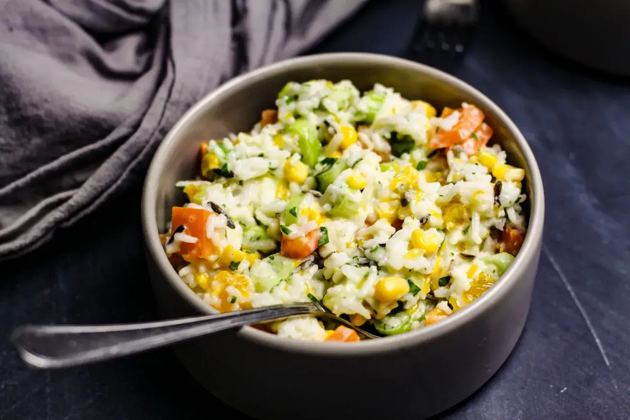 Reissalat mit Mandarinen, Mais und Sellerie, serviert in einer grauen Schüssel mit einer Gabel.