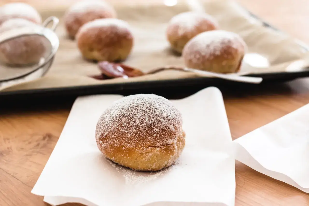 Frisch gebackene Berliner, best&auml;ubt mit Puderzucker, warten auf das F&uuml;llen. Ein Hauch von Zimt und Zucker erinnert an das berliner rezept original.