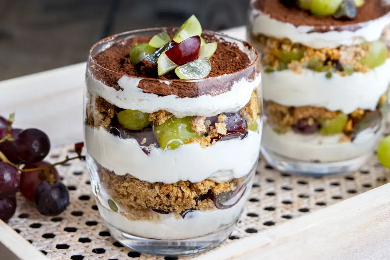 Schichtdessert im Glas mit cremigem Frischkäse, zerbröselten Keksen, saftigen Weintrauben und Kakaopulver. Ein köstliches Weintrauben Cookie Dessert.