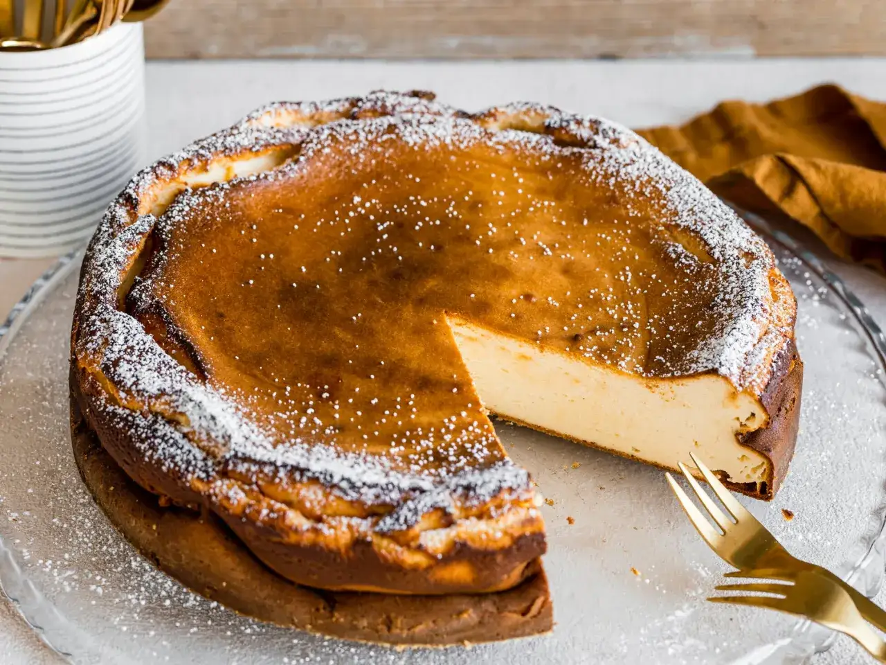 Ein k&ouml;stlicher Quarkkuchen ohne Boden, mit Puderzucker best&auml;ubt, wartet auf seine Verkostung. Ein St&uuml;ck ist bereits angeschnitten.