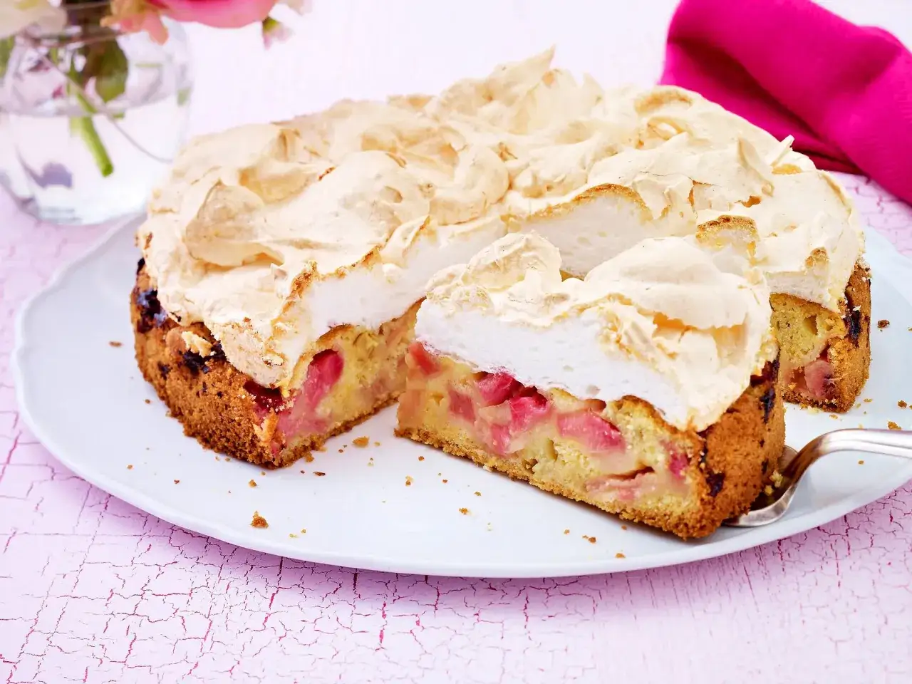 Ein saftiger Rhabarberkuchen mit einer luftigen Baiserhaube, auf einer weißen Platte serviert.