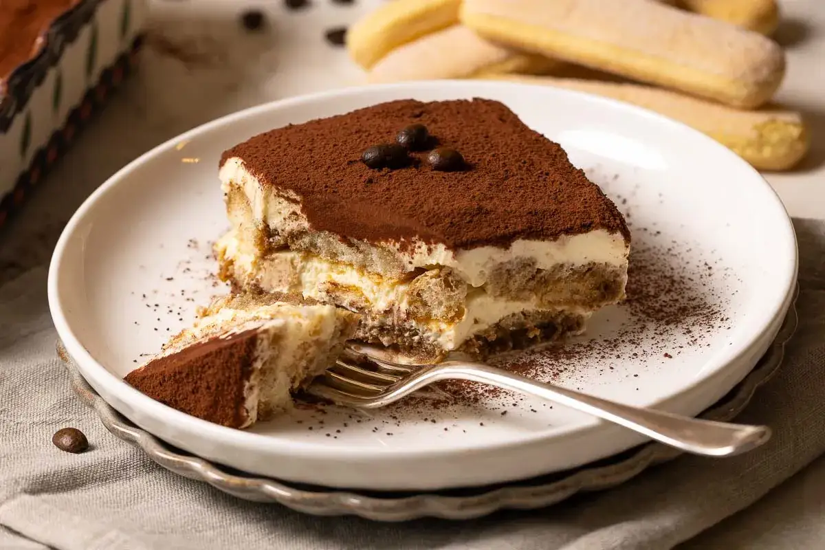Ein Stück cremiges Tiramisu, das nach einem authentischen tiramisu rezept original italienisch schmeckt. Mit Löffelbiskuits, Mascarpone und Kakao bestäubt.