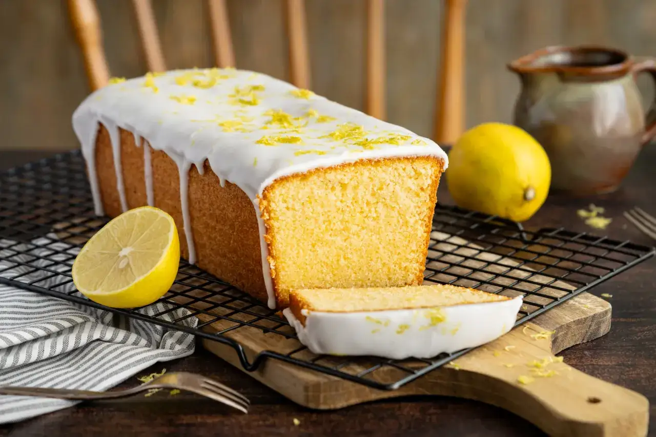 Saftiger zitronenkuchen wie bei Oma, mit Zuckerguss und frischer Zitronenschale bestreut, auf einem Gitter. Daneben liegen Zitronen.