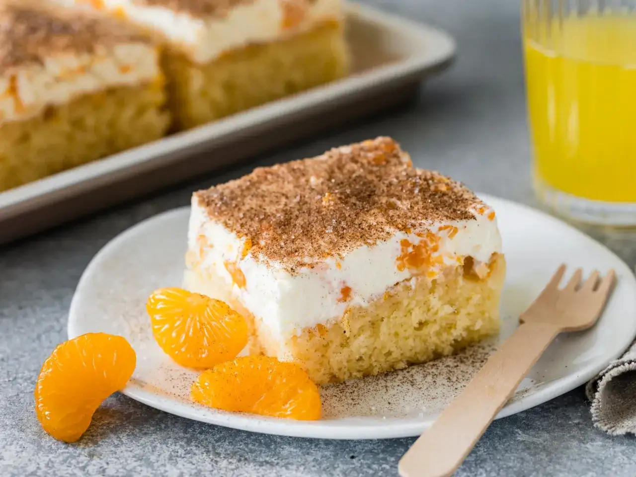Ein Stück saftiger Fantakuchen mit Schmand und Mandarinenstücken, bestreut mit Zimt. Daneben liegen frische Mandarinenspalten.