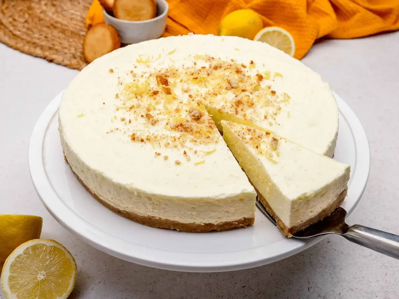 Cremige Philadelphia Torte mit Zitronennote, bestreut mit Krümeln und Zitrusschale. Ein Stück wird gerade serviert.