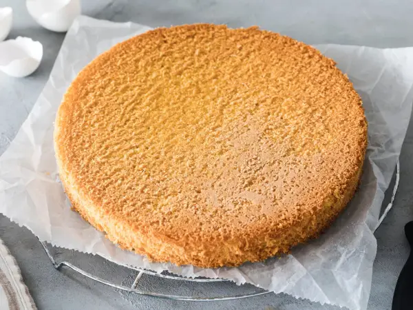 Ein goldbrauner Biskuitboden, perfekt für jedes Biskuitteig Rezept in der Springform. Die Eierschalen im Hintergrund deuten auf die Zubereitung hin.